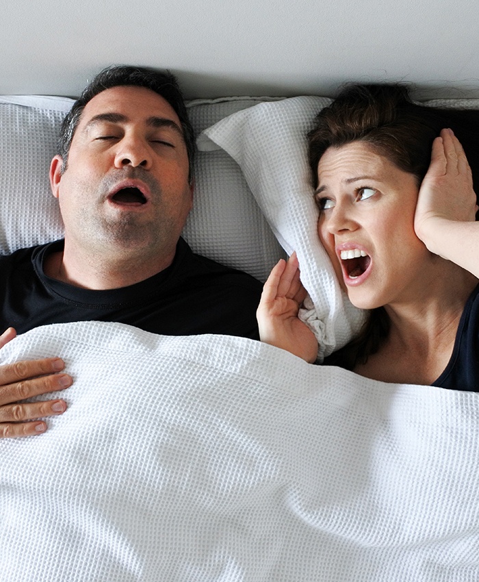 Frustrated woman covering her ears in bed with snoring man