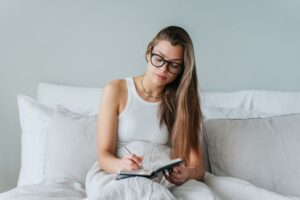 Woman sitting in bed, writing in notebook