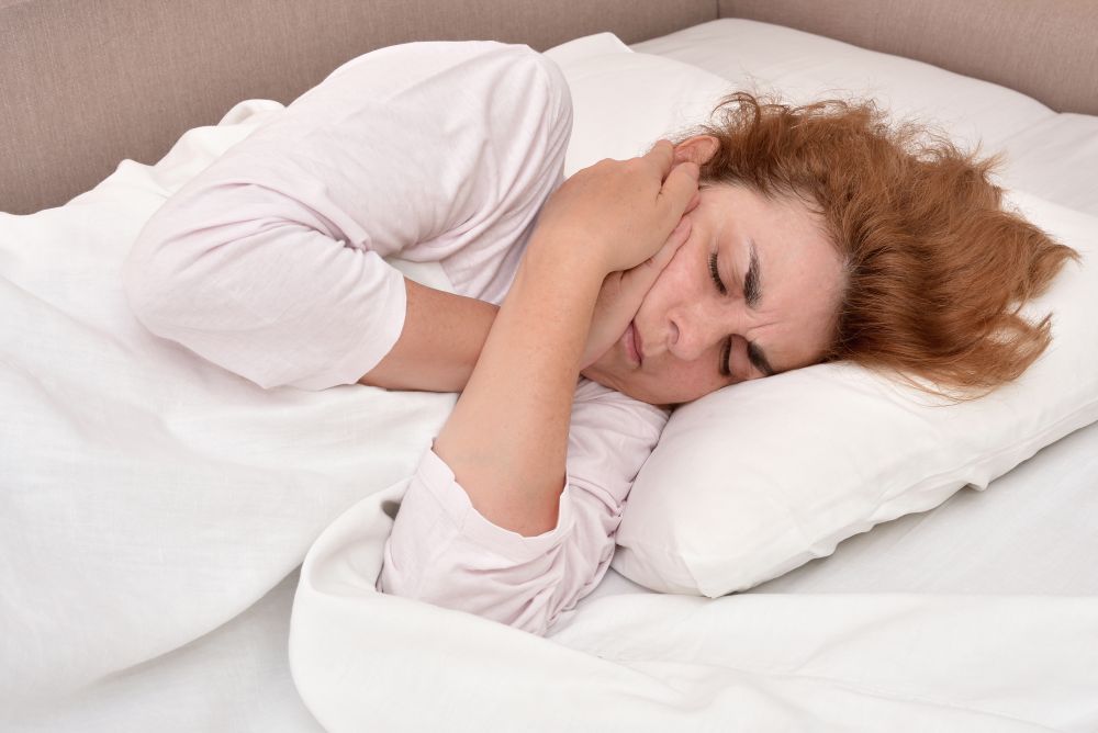 A woman holding her jaw while lying in bed